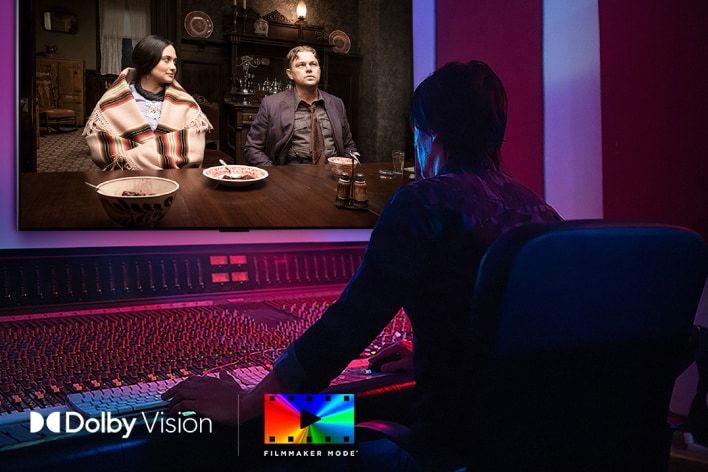 A man sits in front of a mixing board in a sound studio, using a wall-mounted LG G5 OLED 4K Smart TV as a reference monitor.